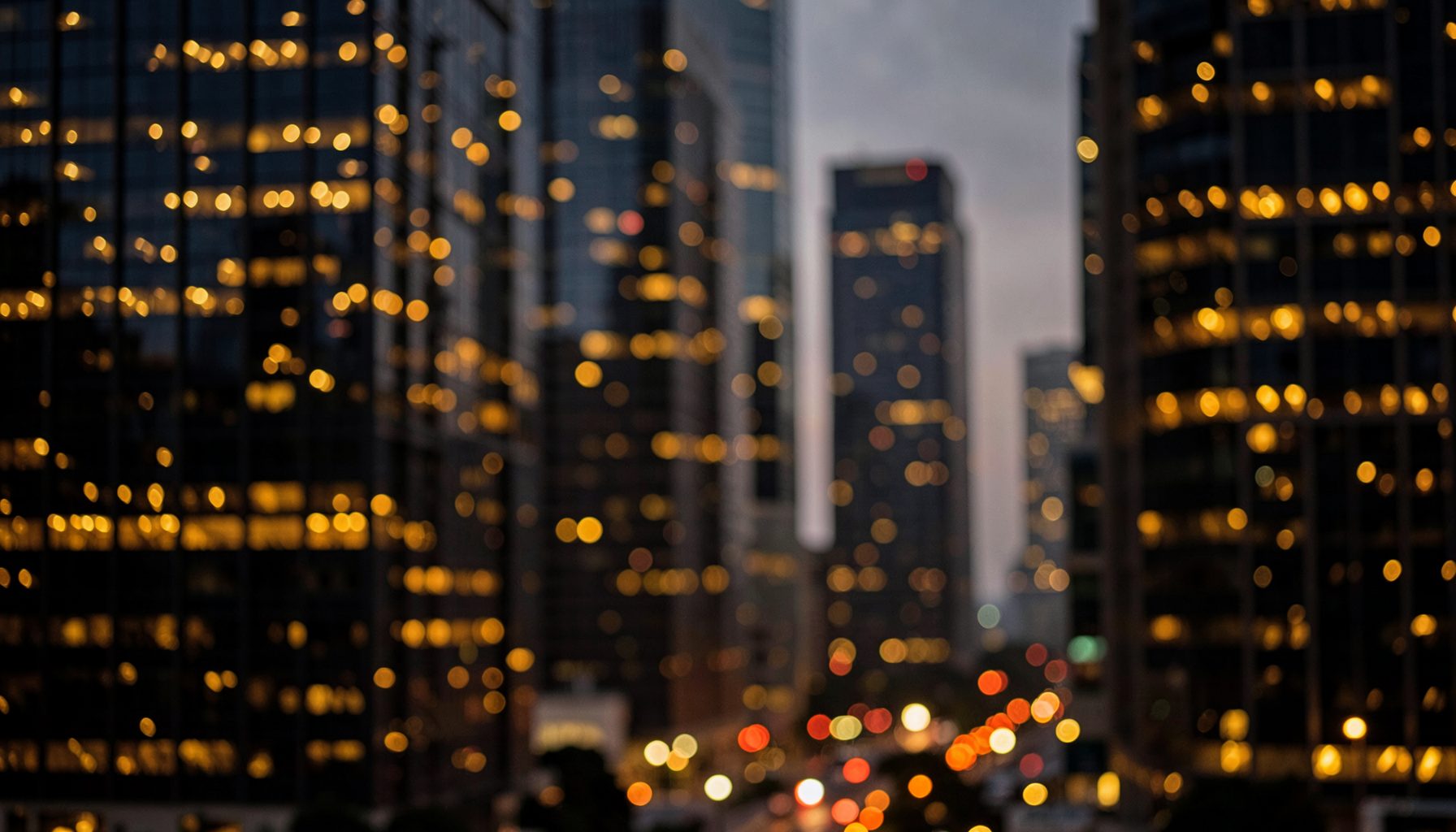 Warm evening city lights reflecting off glass high-rises in a sophisticated urban setting, deep amber and charcoal tones