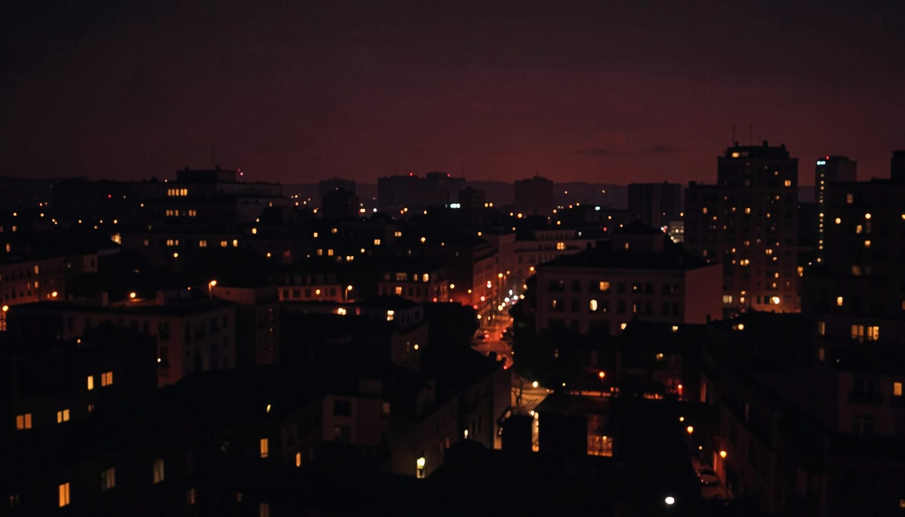 Moody nighttime cityscape in deep red and charcoal tones with soft glowing lights, conveying a discreet upscale evening atmosphere