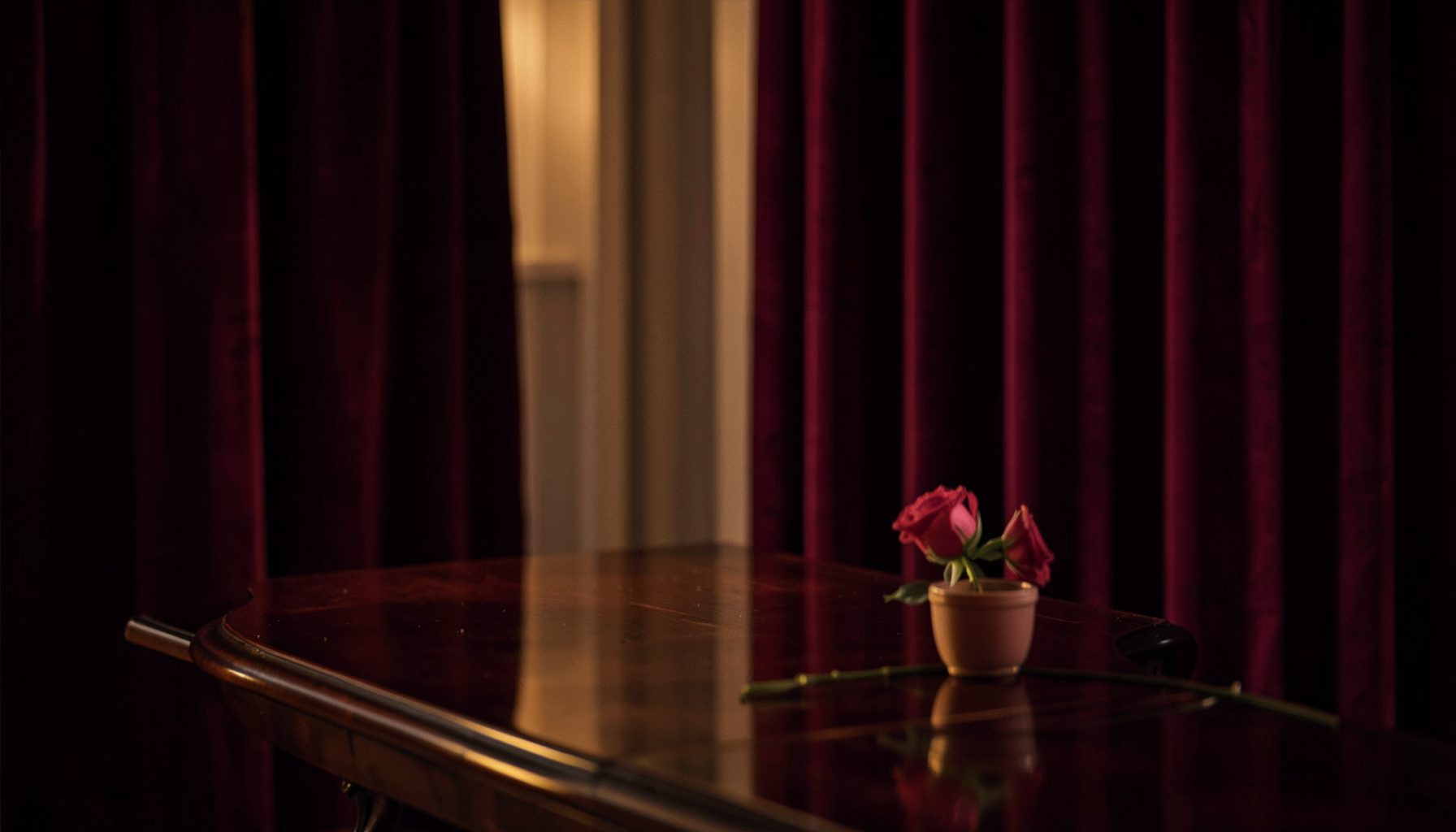 Softly lit interior with deep burgundy velvet drapes, warm amber glow, and a polished dark wood table, intimate and luxurious